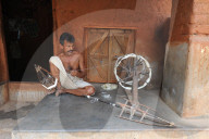 Man on his porch, spinning silk using traditional wooden spinning wheel and stick cages, Nuapatna, Odisha