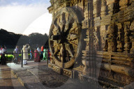 Tourists at sunset by of the 24 carved huge stone chariot wheels carved on 13th century Konark sun temple, Odisha