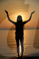 Silhouette of a woman standing by the sea at sunset doing yoga pose and meditation. Kep. Cambodia.
