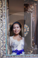 Indonesia, Bali. A Balinese woman in traditional dress looking out from a carved window in a local village