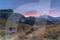 Rear view of woman sitting on grass admiring sunrise on Marmolada and Sass Pordoi, Passo Sella, Dolomites, South Tyrol, Italy