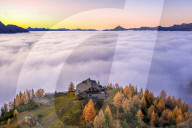 Fog covers the Valmalenco(Val Malenco) with the mountain range of Disgrazia illuminated by sunrise in the background and the Motta mountain hut in the foreground. Valtellina, Lombardy, Italy, Europe.