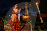 Girl wearing traditional dress and with face painted as catrinal holding candle in graveyard