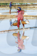 Woman with shoulder pole harvesting the salt fields around the Praek Tuek Chhu River estuary south of the city, Kampot, Cambodia