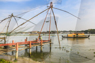 Old Chinese fishing nets & tour boat on the waterfront of Vypin Island with Fort Cochin beyond; Fort Vypin, Kochi, Kerala, India