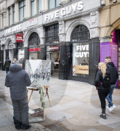 A painter paints a picture of Five Guys in Piccadilly Circus.