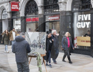 A painter paints a picture of Five Guys in Piccadilly Circus.