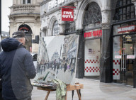 A painter paints a picture of Five Guys in Piccadilly Circus.