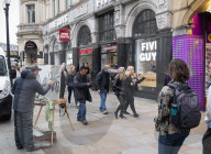 A painter paints a picture of Five Guys in Piccadilly Circus.