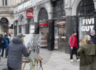 A painter paints a picture of Five Guys in Piccadilly Circus.