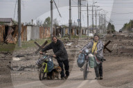 NEWS - Ukraine-Krieg:  Zwei Bewohner Charkiws  stossen ihre Fahrräder auf einer Strasse mit Trümmern