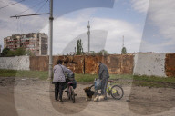 NEWS - Ukraine-Krieg:  Zwei Bewohner Charkiws  stossen ihre Fahrräder auf einer Strasse mit Trümmern