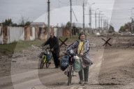 NEWS - Ukraine-Krieg:  Zwei Bewohner Charkiws  stossen ihre Fahrräder auf einer Strasse mit Trümmern