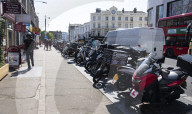 Mopeds are lined up along Wimbledon Broadway with delivery drivers waiting
