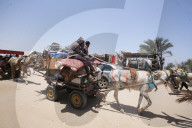Men drive animal-drawn carts loaded with items past the tents and shelters of people displaced by conflict