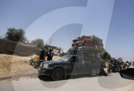Palestinians  ride in the back of a truck loaded with solar panels, cisterns, and other items moving past the tents and shelters