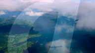 Aerial view through the clouds to the Norwegian fjords, shadow of an airplane on a cloud. Top view from the clouds to the sea bay with coastal hills, Norway - 15 Jun 2024