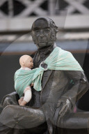 Campaigners tie baby slings to statues in call for better UK paternity leave.