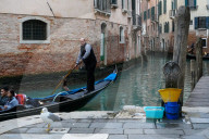 Gondolier With Tourists Navigates Narrow Canal In Venice