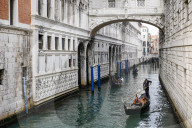 Gondolier With Tourists Navigates Narrow Canal In Venice