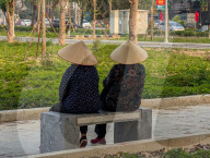 Two Women In Conical Hats Rest On A Bench In A Park In Vietnam