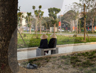 Two Women In Conical Hats Rest On A Bench In A Park In Vietnam