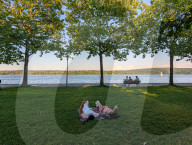 People Relaxing On Benches At The Lake