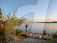 Man Standing And Woman Sitting By The Lake At Sunset