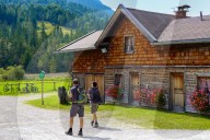 Hikers Passing A Traditional Bavarian Wooden House