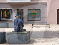 Senior Man Sitting On Stone Block In Front Of Hair Salon