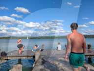 Young People On Lakeside Pier At Lake During Summer Heat 