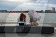Two Women Sitting By The Waterfront With Umbrella