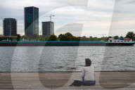 Woman Sitting By The Water Watching A Passing Freight Ship