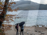 Hikers With Umbrellas On The Rocky Shore Of Lake Eibsee In Rain