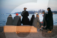 Group Of Young Women Gather On Seawall Bench By Venetian Lagoon At Dusk